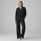 Person wearing a black outfit in a room with clothes in the background