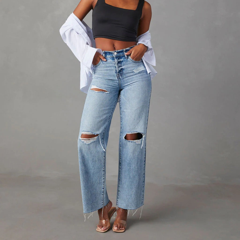 Person wearing ripped blue jeans and a black crop top on a gray background