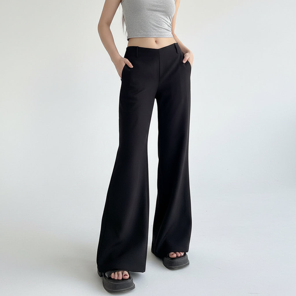 Person wearing black wide-leg pants and a gray crop top against a plain wall.