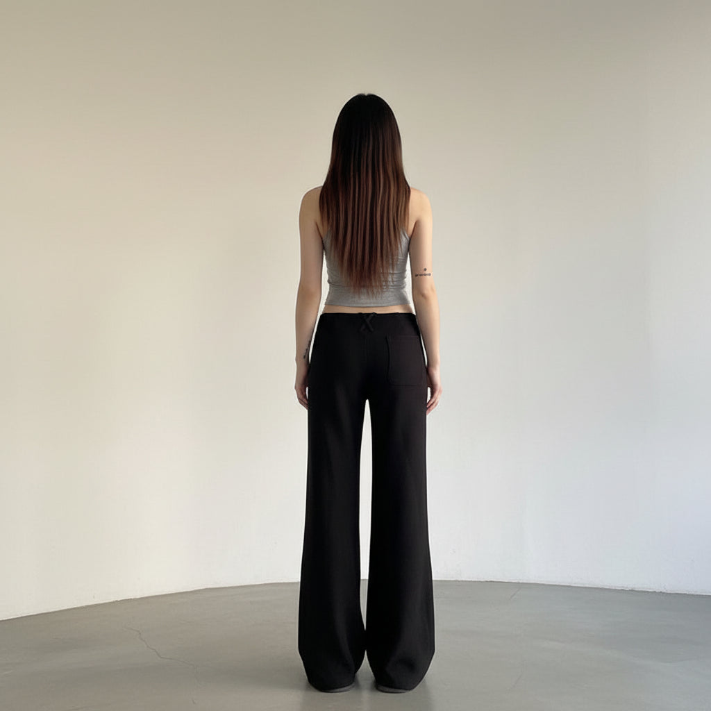 Person wearing black wide-leg pants and a gray top against a plain background