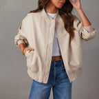 Woman wearing a beige bomber jacket and blue jeans against a gray background