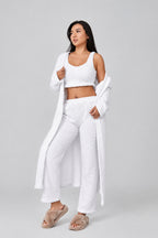Woman wearing a white outfit with a long white coat on a plain background