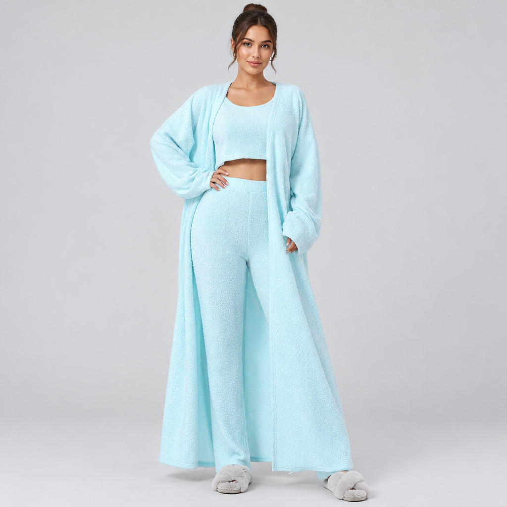 A model wearing a light blue three-piece loungewear set consisting of a cropped tank top, matching high-waisted wide-leg pants, and a long open-front cardigan, styled with beige slippers against a plain white background.