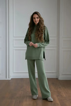 Woman wearing a green outfit standing in a room with white paneled walls.