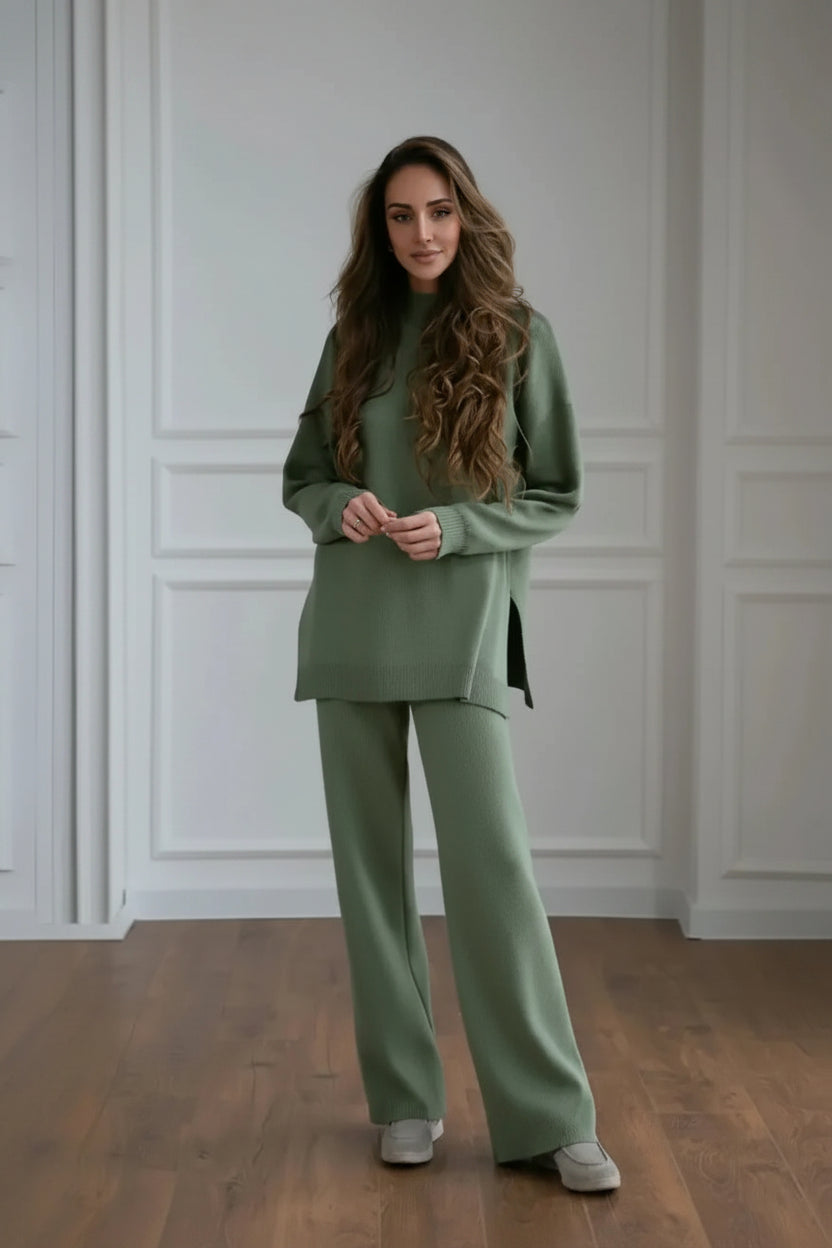 Woman wearing a green outfit standing in a room with white paneled walls.