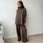 Woman wearing a brown knit outfit standing against a white wall.