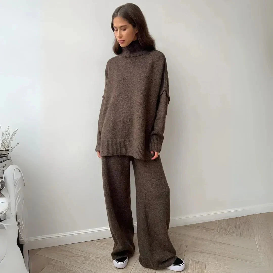 Woman wearing a brown knit outfit standing against a white wall.