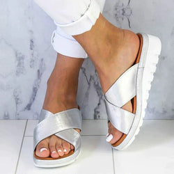 Silver sandals worn with white pants on a marble floor