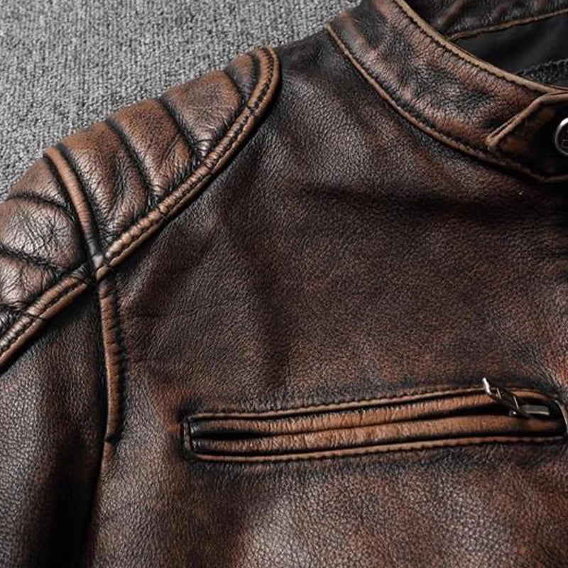 Close-up of a brown distressed leather jacket showing the textured leather, ribbed shoulder detailing, and a horizontal zippered pocket.