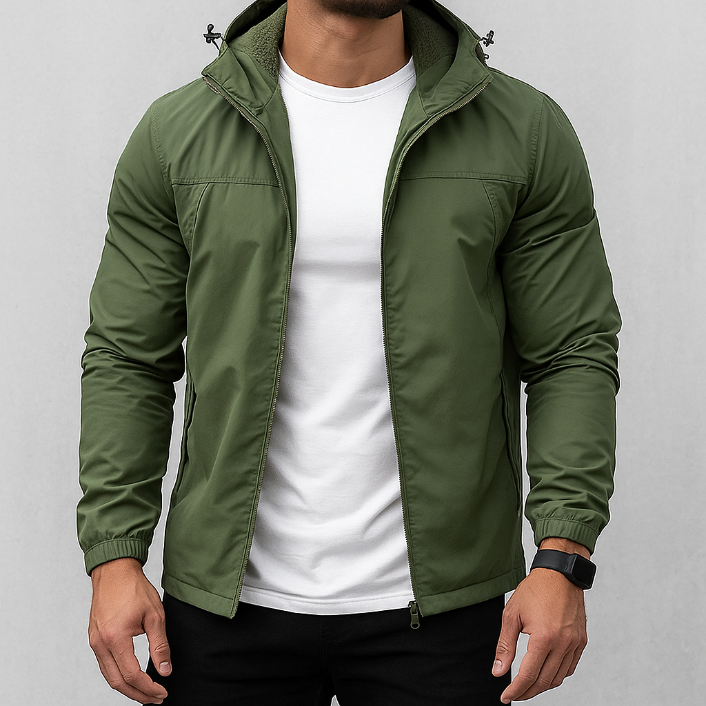 A man wearing an olive green lightweight zip-up hooded jacket over a white t-shirt and black pants, shown from the neck down against a light gray studio background.
