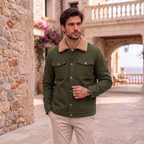 A man wearing an olive green military-style jacket with a beige sherpa collar, standing in a stone courtyard.