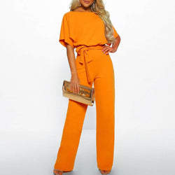 Woman wearing an orange jumpsuit holding a gold clutch against a white background