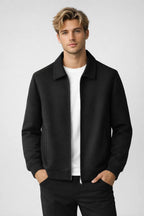 Man wearing a black jacket over a white shirt on a light gray background