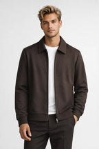Man wearing a brown jacket over a white shirt on a light gray background