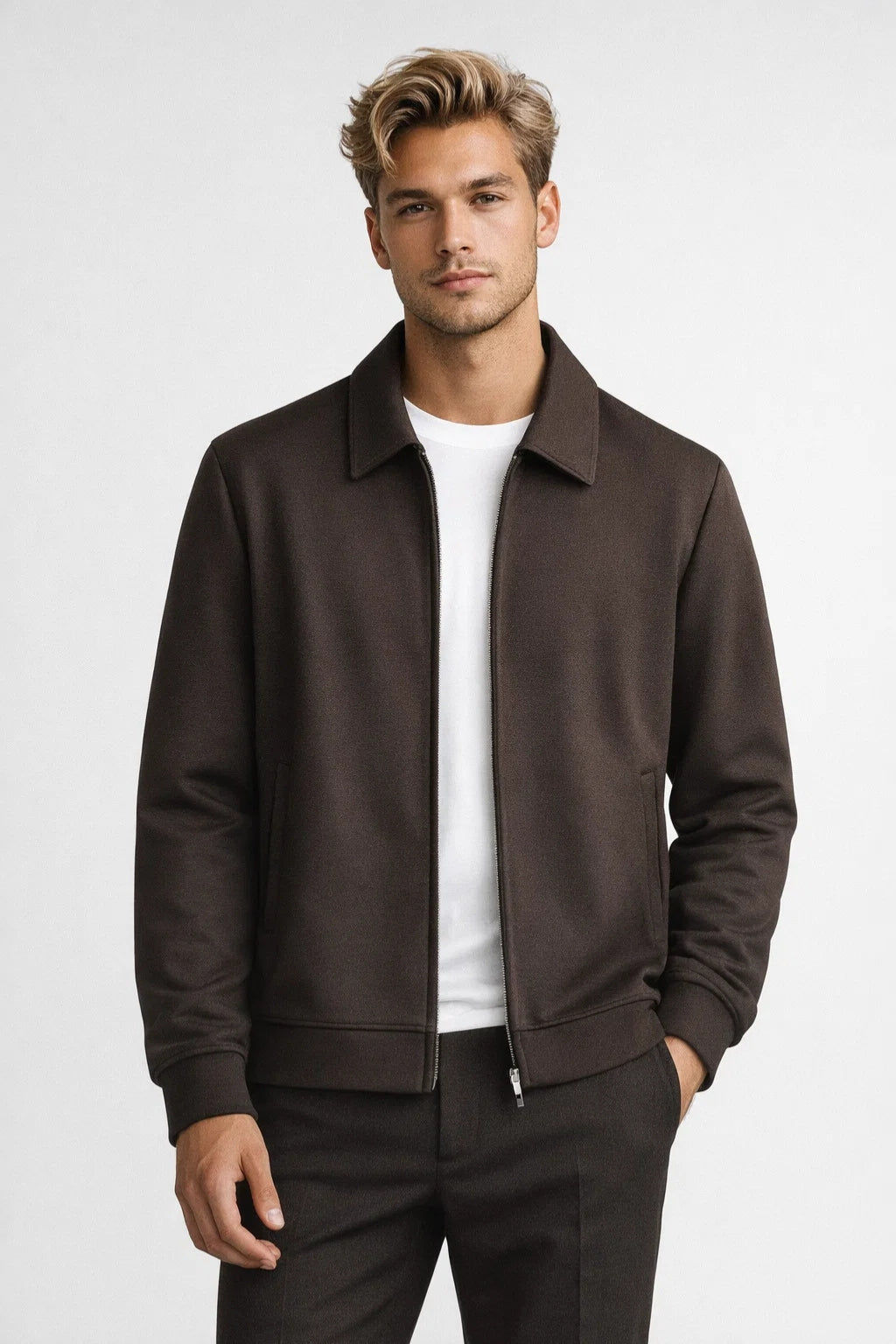 Man wearing a brown jacket over a white shirt on a light gray background