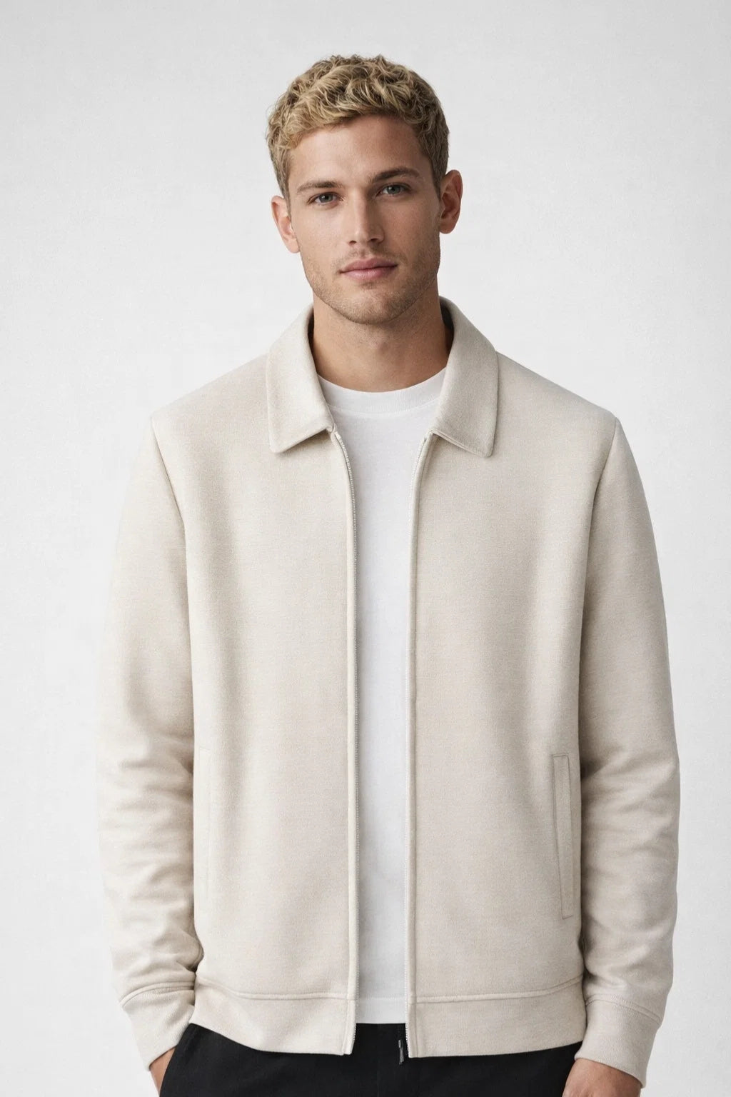 Man wearing a beige jacket over a white shirt on a light gray background