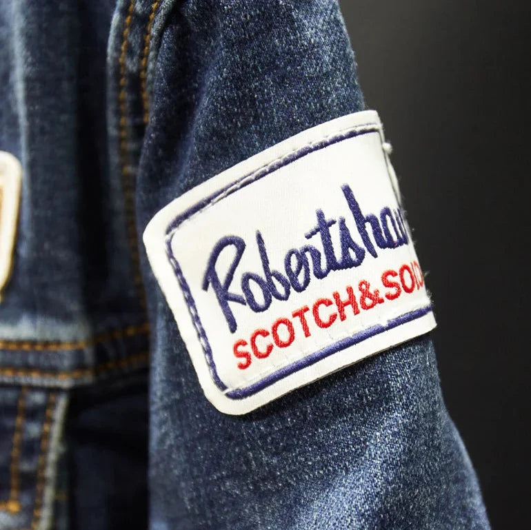 Close-up of a denim jacket sleeve featuring a white embroidered patch with the brand name 'Robertshaw SCOTCH&SOUL' in blue and red lettering.