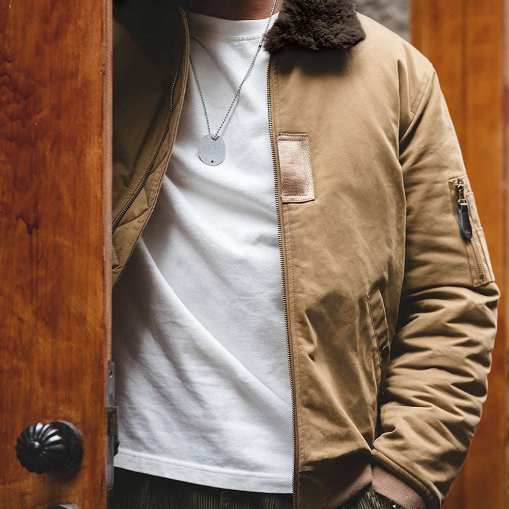 Person wearing a beige jacket over a white shirt with a wooden door background