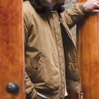 Person wearing a brown quilted jacket with fur collar, standing next to a wooden door.