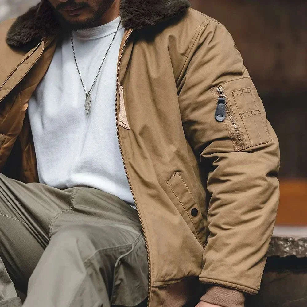 Person wearing a brown jacket with fur lining, sitting outdoors.