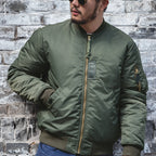 Man wearing a green bomber jacket against a brick wall.