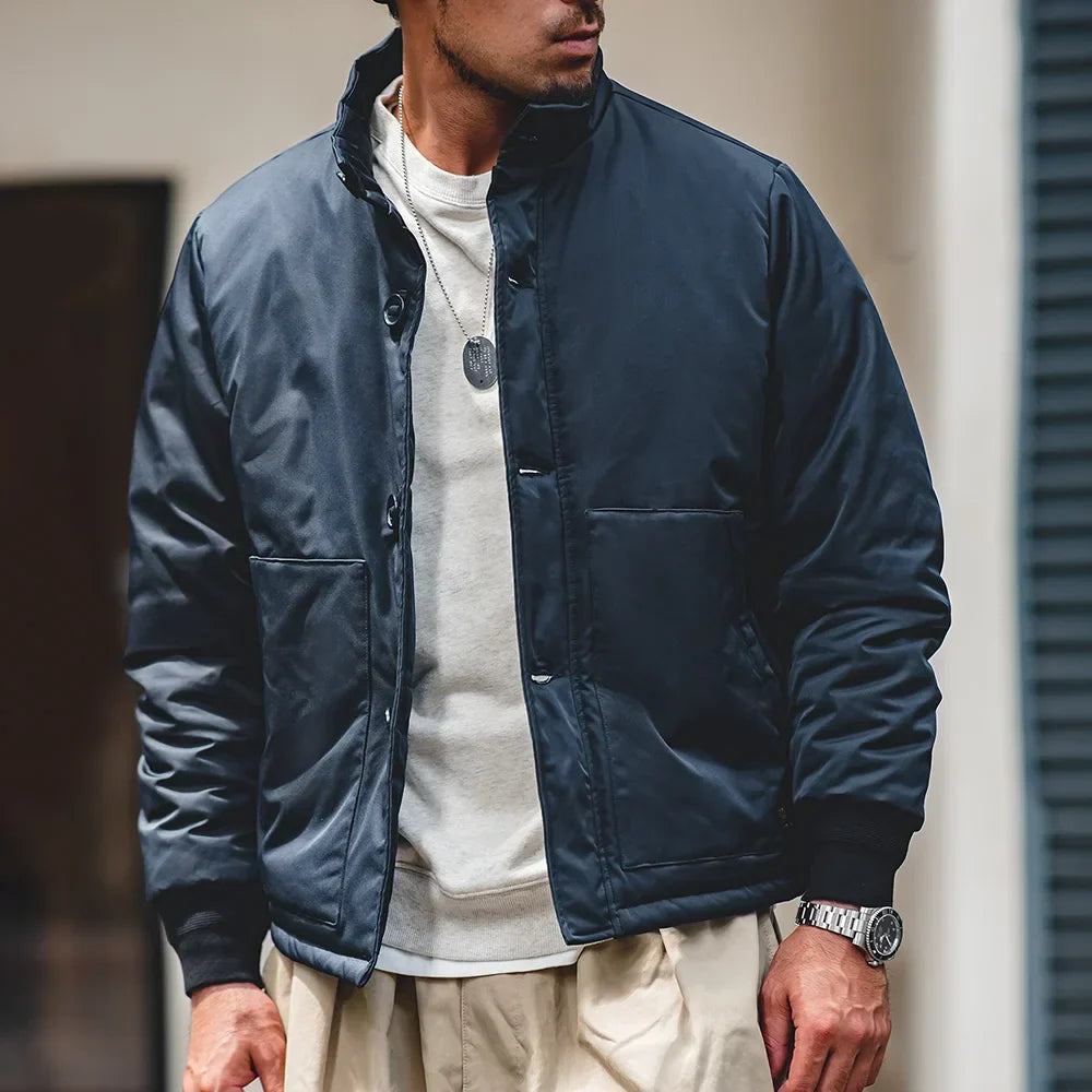 Man wearing a navy blue jacket over a white shirt, standing indoors.