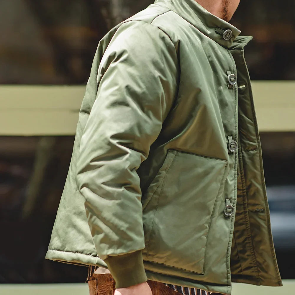 A close-up side view of a person wearing an olive green padded jacket with a high collar, front button closure, and large front patch pocket.