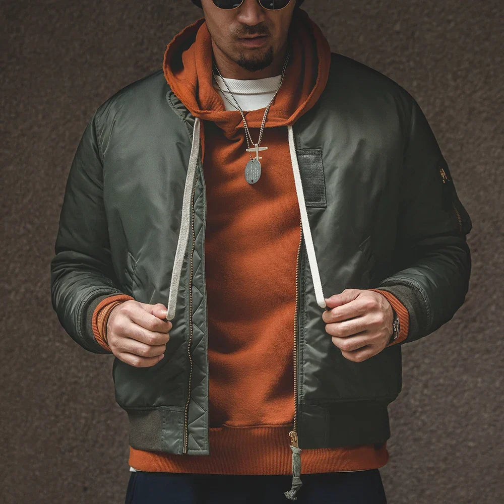 Man wearing a green jacket over an orange hoodie with a brown background