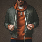 Man wearing a green jacket over an orange hoodie with a brown background