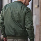 Person wearing a green bomber jacket with a blurred background