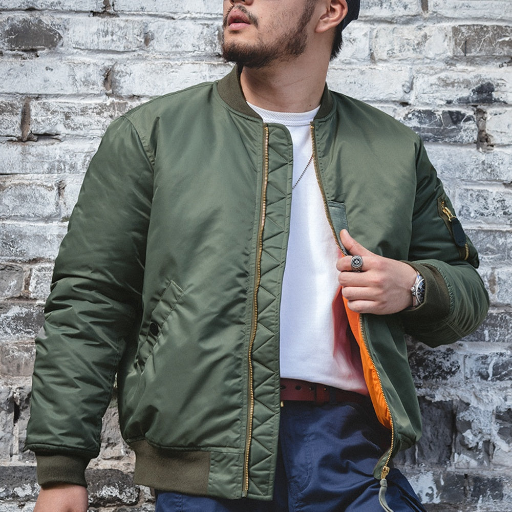 Person wearing a green bomber jacket against a brick wall.