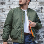 Person wearing a green bomber jacket against a brick wall.