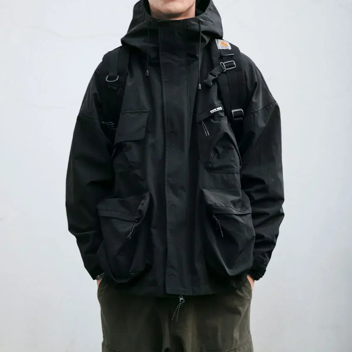Person wearing a black jacket with a backpack on a plain background