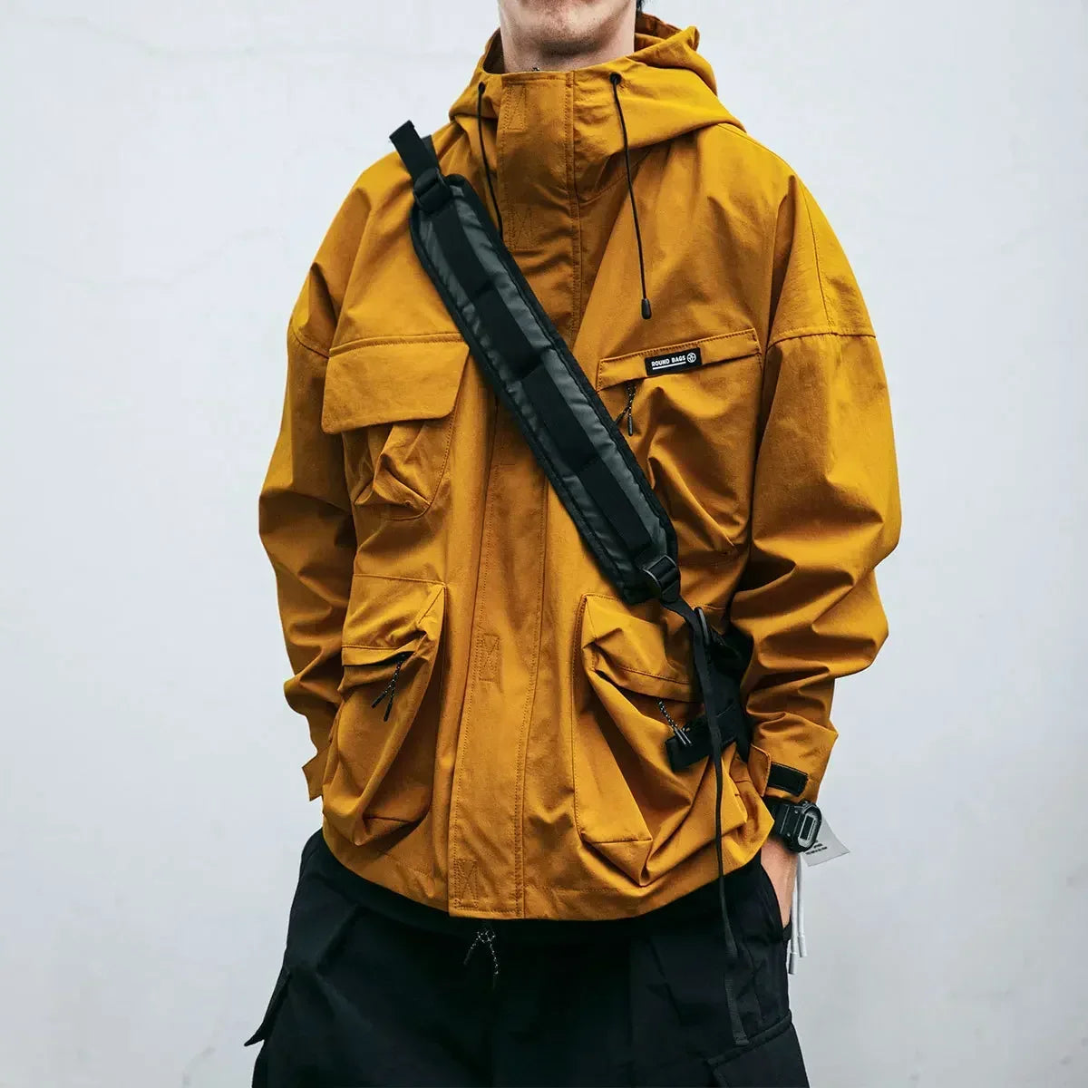 Person wearing a mustard yellow jacket with a black strap over a white background