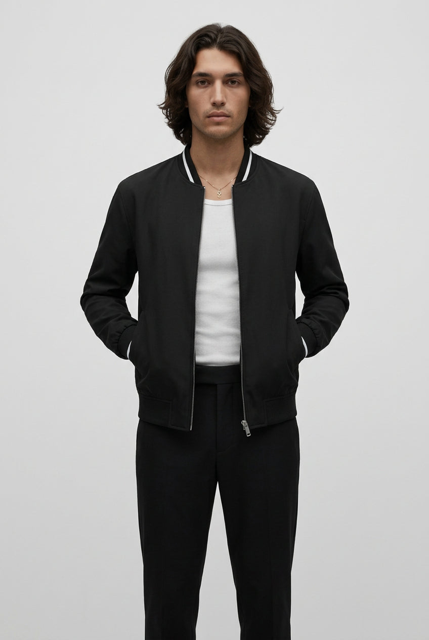 Man wearing a black bomber jacket over a white shirt on a plain background