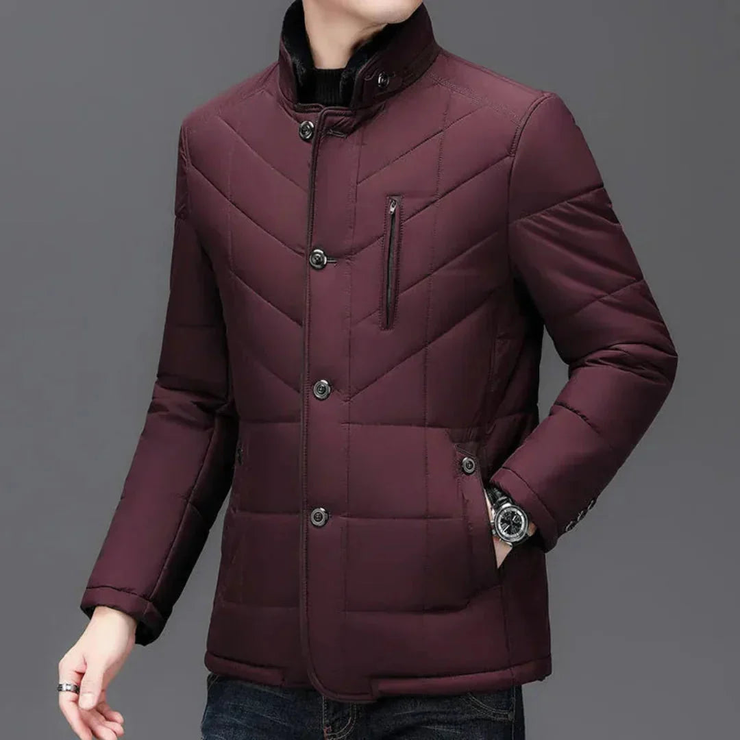 A man wearing a quilted men's winter jacket in deep burgundy. The jacket features a stand-up collar, a button-front closure, diagonal quilting, and zippered pockets, shown against a solid gray background.