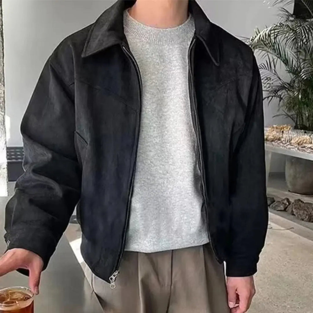 Person wearing a black jacket over a gray sweater, standing indoors.
