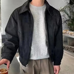 Person wearing a black jacket over a gray sweater, standing indoors.