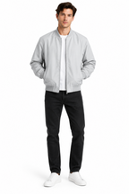 A man modeling a light gray zip-up bomber jacket over a white t-shirt, black jeans, and white sneakers, photographed against a seamless white studio background.