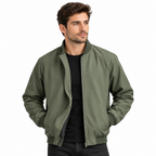 A man wearing an olive green bomber jacket over a black t-shirt and dark jeans, photographed against a solid white background.