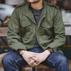 Person wearing a green jacket and blue jeans sitting on a bench.
