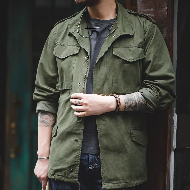 Person wearing a green jacket with tattoos on arms, standing against a dark background.