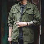 Person wearing a green jacket with tattoos on arms, standing against a dark background.