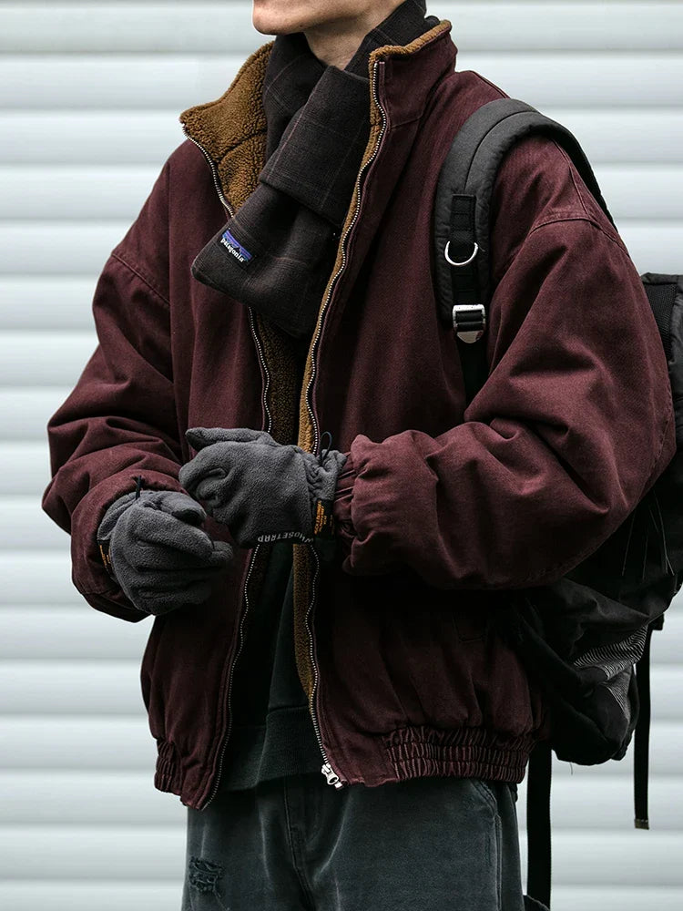 Person wearing a maroon jacket with a fur-lined hood and carrying a backpack against a gray background