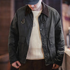 Person wearing a dark green jacket over a cream sweater with a blurred background