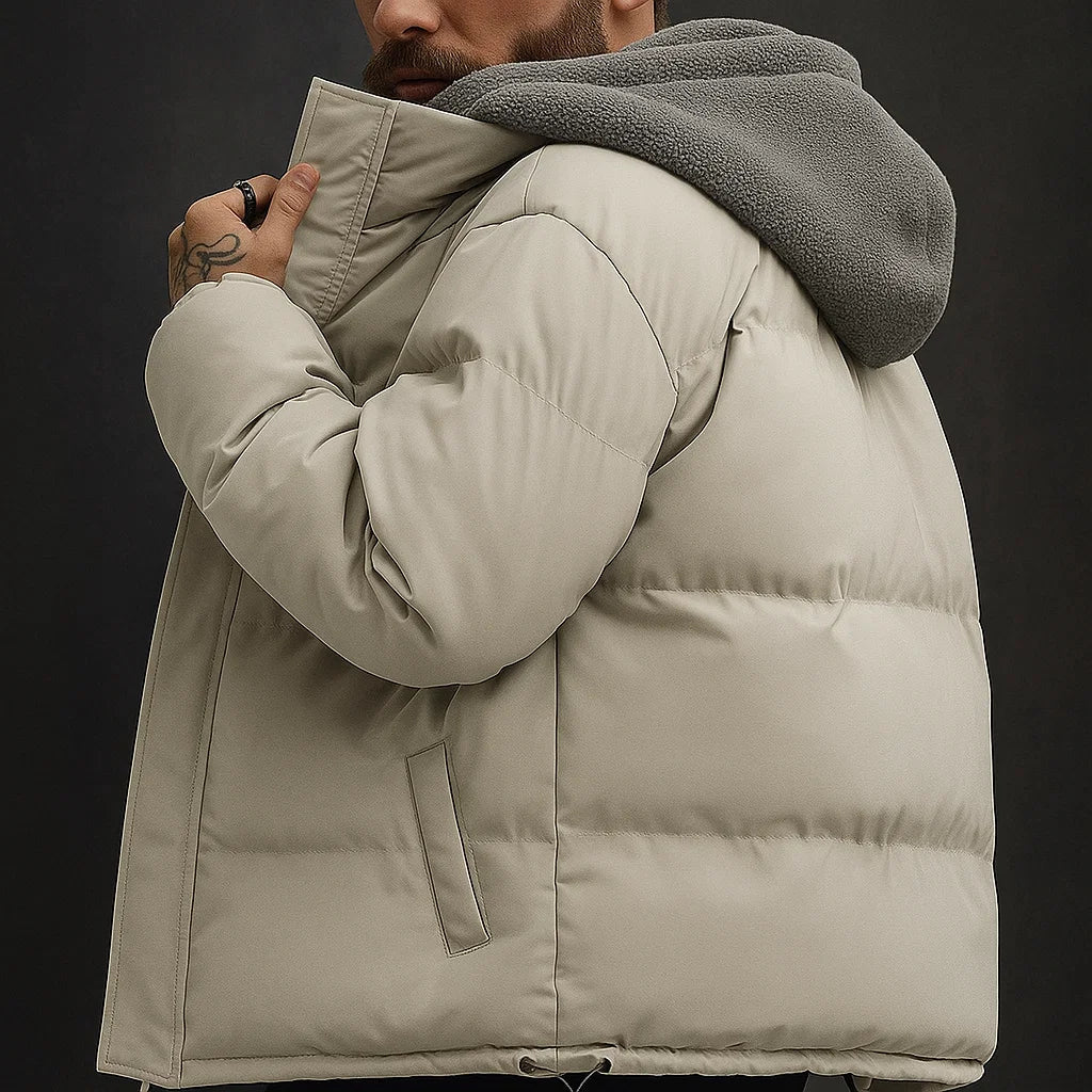 Person wearing a beige puffer jacket with a gray hood against a dark background