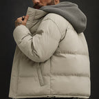 Person wearing a beige puffer jacket with a gray hood against a dark background