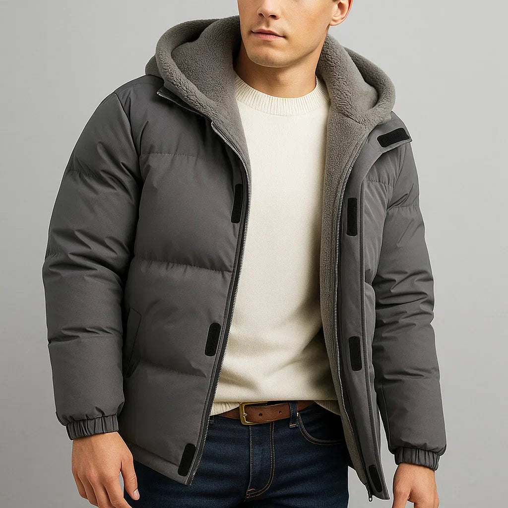 Man wearing a gray puffer jacket with a hood on a gray background