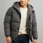 Man wearing a gray puffer jacket with a hood on a gray background