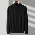 A black ribbed knit zip-up sweater with a mock neck collar, hanging on a wooden hanger against a light gray wall with soft diagonal shadows.